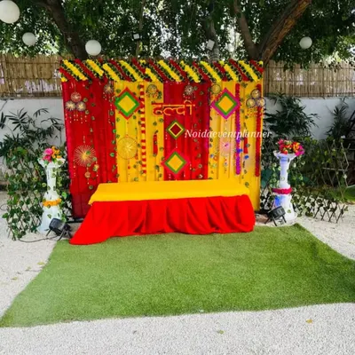 A classic Haldi ceremony setup with a bright yellow and red backdrop, decorated with marigold flowers and traditional hangings for a festive feel.