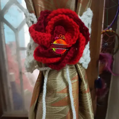 An elegant curtain tie-back featuring a large, intricately crocheted red rose on a white band. This design adds a touch of classic romance to any window dressing.