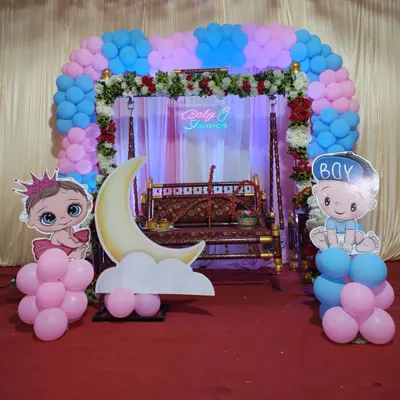A beautiful setup for a traditional baby shower or Dohale Jevan. It features a decorated swing (jhula), a pink and blue balloon arch, and cute baby cutouts to welcome the little one.