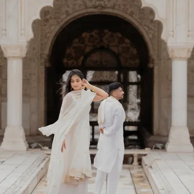 Posed against the intricate archways of a Delhi fort, this shot captures a sense of quiet elegance. The bride's flowing white outfit and the groom's classic kurta create a timeless portrait.