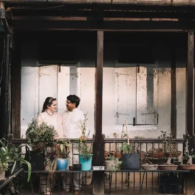 This was a beautiful moment captured at the groom's ancestral home, an old 'vada' in Pune. The rustic charm of the balcony, with its weathered shutters and collection of plants, provided a perfect, personal setting for this post-wedding portrait.