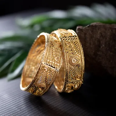 A detailed product shot of intricately designed gold bangles. I used a rock and natural leaf to create an earthy, rustic setting that contrasts beautifully with the polished gold.