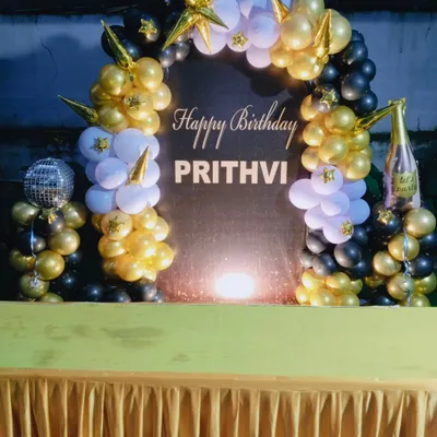 A stylish black, gold, and white balloon arch for Prithvi's birthday, complete with a shimmer backdrop, star-shaped balloons, and a champagne bottle prop.