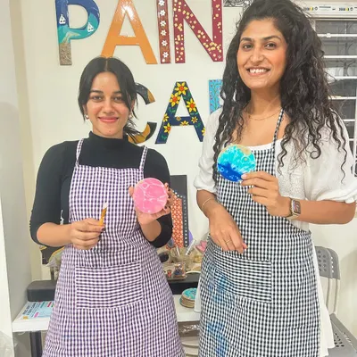 Two friends having a great time at the studio, showing off the coasters they painted.