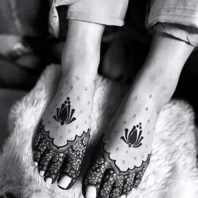 An artistic black and white photograph of our lotus foot mehandi. The design features a bold lotus motif on the top of the foot with delicate floral work covering the toes.