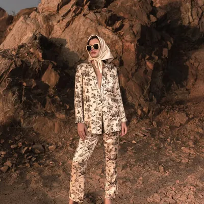 A full-length shot of a modern pantsuit against a rugged, rocky backdrop. This composition contrasts the sharp tailoring of the outfit with the raw texture of the outdoors, creating a striking image for a fashion campaign.