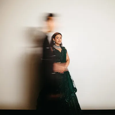 An artistic sangeet portrait using motion blur to create a dynamic and dreamy effect. The bride stands radiant and in focus while the groom is a blur of movement beside her, symbolizing a world that moves fast while their love stands still.