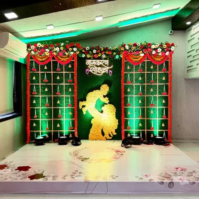 A traditional 'Namkaran Sohala' stage setup for Eraya’s ceremony. We used a green grass wall panel decorated with marigold flowers and hanging bells, with a mother and child silhouette as the centerpiece.