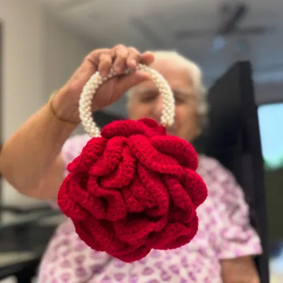 Our signature Peony Bag in a stunning bright red, held by Dadi. This bag is a work of art, featuring a pearl handle and intricate petal-like crochet work.