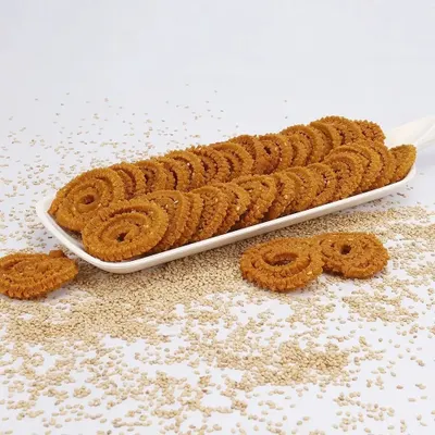 A studio shot of traditional Indian chakli, neatly arranged on a white platter with scattered sesame seeds to highlight the key ingredient. This is a classic e-commerce product shot for savory snacks.