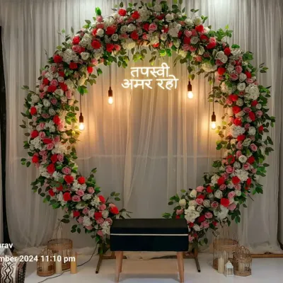 A full circular arch made of red and white flowers for a Tapasvi ceremony at home. The neon sign and hanging Edison bulbs add a modern touch to the traditional setup.