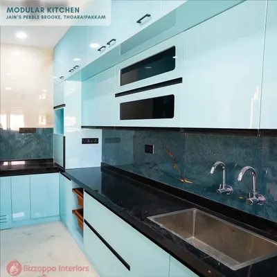This modular kitchen at Jain's Pebble Brooke features stunning light blue lacquered glass cabinets. The cool tone is beautifully contrasted with a dark green marble-patterned backsplash and a black granite countertop for a sophisticated finish.