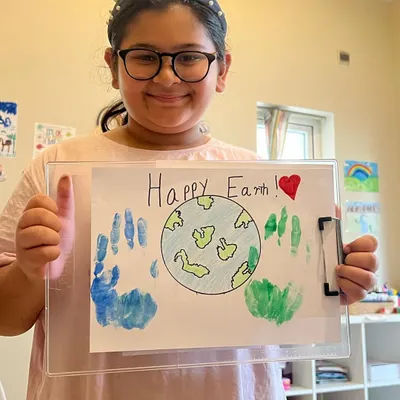 Spreading Earth Day vibes! This young artist is proud of her "Happy Earth" artwork, complete with handprint continents. It's a great way to learn about preserving our beautiful planet.