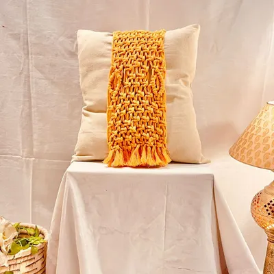 This mustard yellow macrame cushion tie-back features an intricate basket-weave pattern and a fringed bottom. It’s designed to wrap around a plain cushion, instantly transforming it into a decorative statement piece.