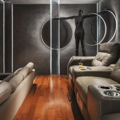 This private home theater in a Kadapa residence is the ultimate in bespoke entertainment. The design features dramatic vertical and circular lighting, dark textured walls for optimal viewing, and a striking sculpture as a centerpiece.