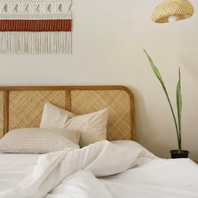 The design of this bedroom is centered on natural textures. The woven cane headboard is complemented by a handcrafted macrame wall hanging, creating a tactile and visually soothing focal point above the bed.