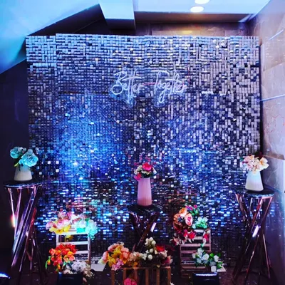 A glamorous photo booth featuring a silver shimmer wall that sparkles under blue lighting. A 'Better Together' neon sign adds a romantic and modern touch, making it a perfect spot for couple and guest photos.