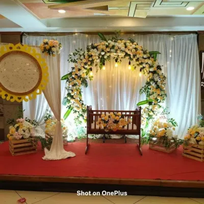 A full view of a naming ceremony stage, showing the decorated cradle under a soft floral arch. The setup includes matching flower arrangements in rustic wooden crates, creating a cohesive and charming look.