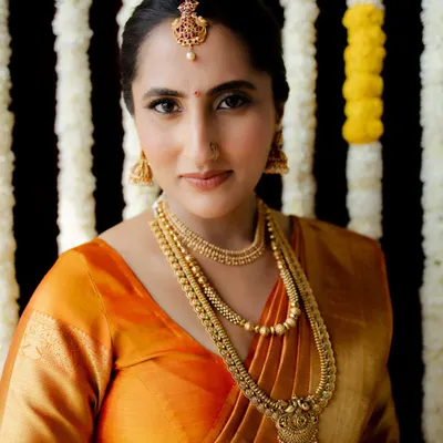A stunning bridal portrait of a South Indian bride in a traditional orange Kanjivaram saree. Her calm demeanor and elegant jewelry make for a timeless and graceful image.