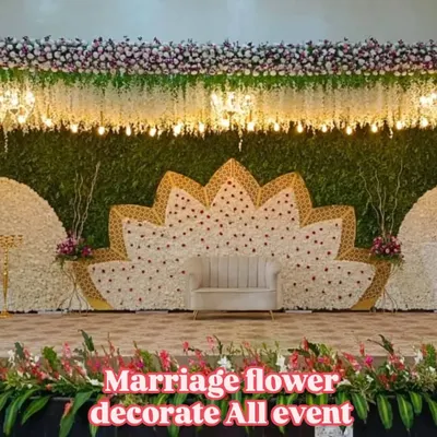A beautiful and modern stage decoration for a wedding reception. The centerpiece is a large, intricate lotus pattern made from white and pink flowers, complemented by a simple, elegant sofa for the couple.