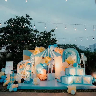 A spectacular carnival theme for a "first birthday" celebration. This outdoor setup features a custom stage, light-up name blocks, a Ferris wheel prop, and a circus tent, all under romantic string lights.