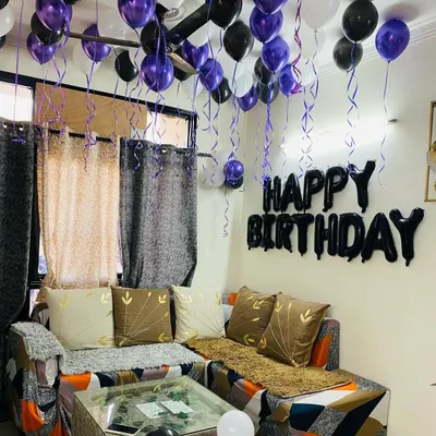 A simple and classic birthday decoration for a living room. This setup includes purple, black, and white balloons on the ceiling and a "Happy Birthday" foil banner on the wall.