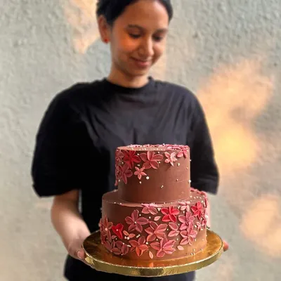 Sanjana from our team holding one of her beautiful creations. This two-tiered chocolate wedding cake is decorated with hand-piped buttercream flowers, a testament to the love and care we put into every order.