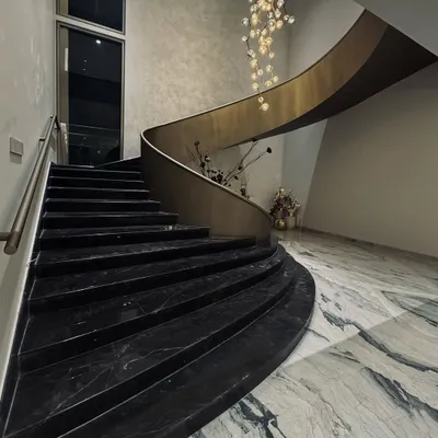 A view of the sculptural staircase from the ground floor. The sweeping curve of the black marble steps and the brass-finished balustrade create a powerful statement of modern elegance.