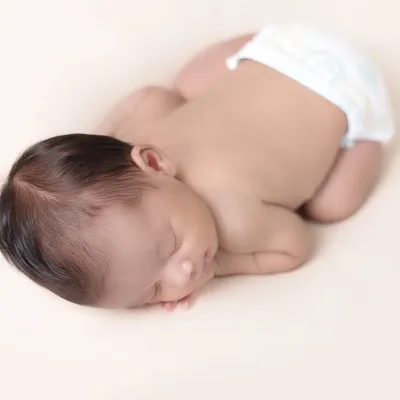 The simple, pure beauty of a newborn. This minimalist pose focuses on the tiny, perfect details of your baby, from their curled fingers to their peaceful expression, creating a timeless and classic newborn portrait.