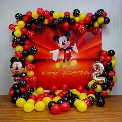 A classic Mickey Mouse theme for a 2nd birthday. This decoration features a large printed backdrop of Mickey, framed by a balloon garland in his signature red, yellow, and black colors, including some with polka dots. A large number '2' foil balloon and a Mickey Mouse balloon figure complete the look.