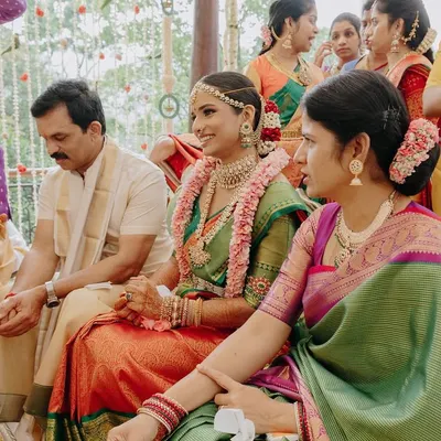 A candid moment from a Mahuratham ceremony, with the bride seated between her parents. Her traditional makeup look, featuring defined eyes and radiant skin, ensures she looks perfect from every angle.