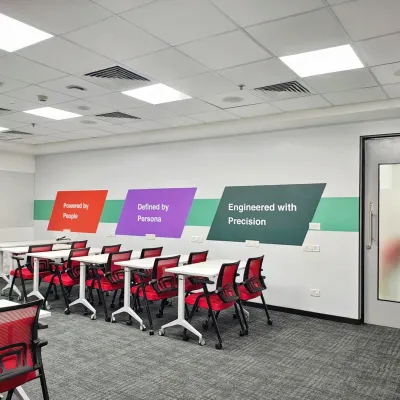 A flexible training room at the Mindsprint office with movable tables and stackable chairs. The wall graphics reinforce the company's core principles: "Powered by People, Defined by Persons, Engineered with Precision."