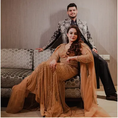 A powerful and glamorous portrait of a couple in stunningly detailed outfits, exuding confidence and elegance in a posed indoor setting.