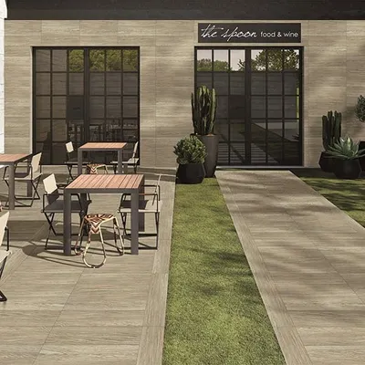 We help businesses create inviting outdoor spaces for their customers. For this cafe, we designed a clean and modern patio area, integrating strips of green lawn with wood-look tile flooring to define the space and add a touch of nature.