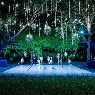A magical cocktail party setup with a custom dance floor set under a canopy of fairy lights. The hanging floral arrangements and chandeliers add a touch of romance and sophistication to the starry night.