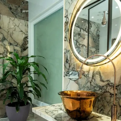 This powder room is designed to make a statement, with floor-to-ceiling dramatic marble, a hammered copper vessel sink, and a backlit mirror. The design composes stone, metal, and light into a functional work of art.