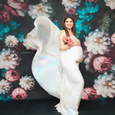 The flowing fabric of this white gown creates a sense of movement and drama against the dark floral backdrop. This is a signature shot from my fine art maternity collection.