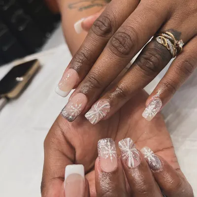 A winter wonderland on your fingertips. We created this elegant holiday look with a classic French manicure base and added delicate, hand-painted white snowflakes with a touch of glitter.