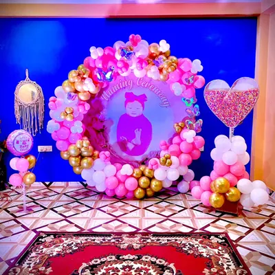 A stunning decoration for a Naming Ceremony. This setup features a personalized backdrop with the baby's photo, framed by a beautiful ring of pink, white, and gold balloons with butterfly accents.