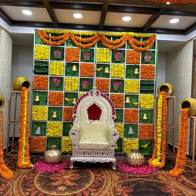 This is a complete traditional stage setup, ideal for a Haldi or Mehendi ceremony. It features a checkered backdrop made of green panels and marigold flower strings, complemented by decorative pots (matkas) and a classic throne-style seat.