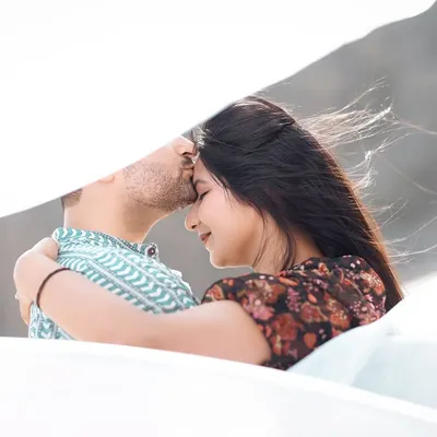 A gentle forehead kiss, with a soft white cloth creating a dreamy, veiled effect. This is a very intimate and artistic portrait.