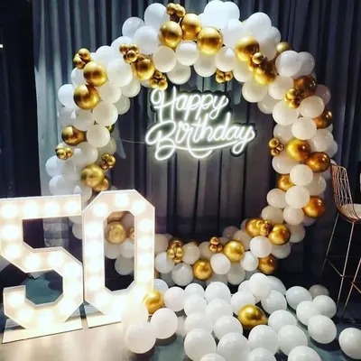 This 50th birthday backdrop features a classic white and gold balloon ring. The large, illuminated marquee '50' stands next to it, creating a glamorous and celebratory photo opportunity for the milestone event.