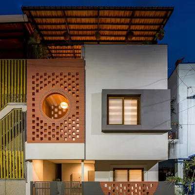 The facade of the Mathrukrupa residence at dusk. The perforated terracotta brick screen, a modern take on the traditional jali, is a key element for passive cooling, allowing air to flow while filtering harsh sunlight.