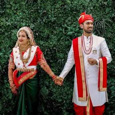 A classic portrait of a Marathi couple, Aditya and Divya. The bride's traditional Nauvari saree and the groom's 'pheta' (turban) are beautifully captured against a lush green backdrop, showcasing the elegance of a Maharashtrian wedding.