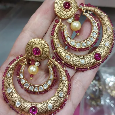 A close-up of our traditional jewellery. These are heavy, gold-plated chandbali earrings with intricate carvings, uncut stones, and ruby-colored beadwork.