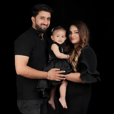 A classic standing portrait against a black background puts all the emphasis on the family. This composition with the parents holding their young daughter creates a feeling of warmth, protection, and love.
