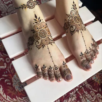 A delicate and modern foot mehendi design. This style features a central motif on the top of the foot with patterns extending to the toes and a matching anklet band.