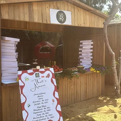 This is my rustic wooden kiosk, set up for an outdoor event. It features my portable red oven, stacks of pizza boxes, and a menu, creating a charming, market-style feel.