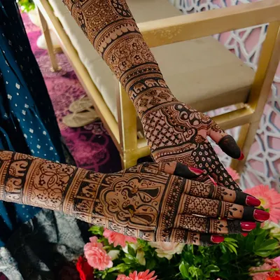 A stunning full-arm bridal design where every detail matters. The composition is set against a beautiful floral backdrop, highlighting the artistry of the henna.