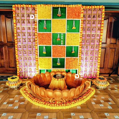 A traditional Haldi ceremony setup featuring a custom-made lotus-shaped seating area. The backdrop is a vibrant grid of green banana leaves and marigold flowers, accented with temple bells for an authentic touch.